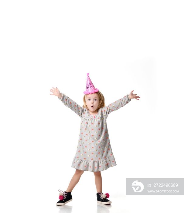 Young blond girl in birthday party princess hat surprised emotions  with hands spread up isolated on a white