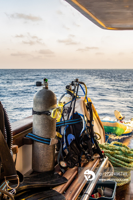 Diving gear with tanks, BCDs,  regulators, weight belts assembled, on a diving boat with sea view in the background, Red Sea, Sudan, portrait view.