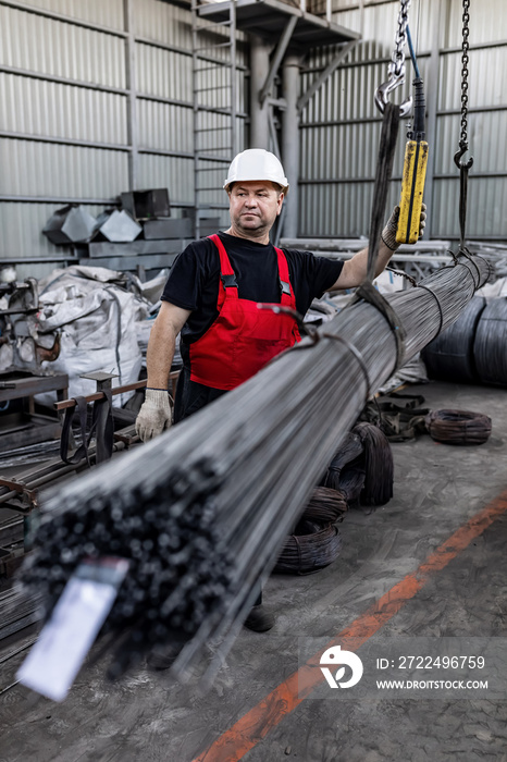 A factory worker loads metal rods with a crane beam. Iron products in the warehouse.