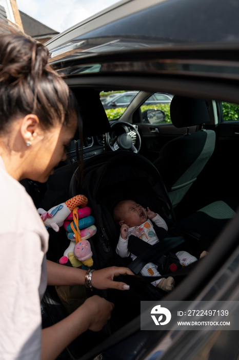 Mother fastening seat belts in car safety seat in car