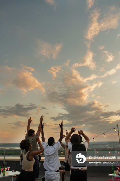 Young multiracial people raising arms while dancing at rooftop party