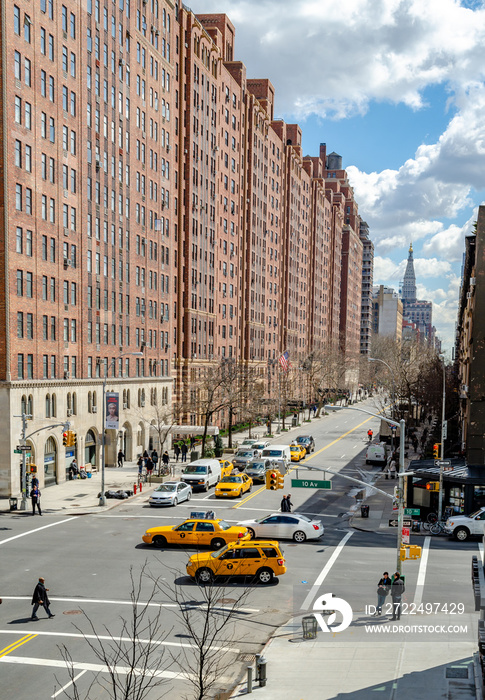 Crossroads at Chelsea, New York City with lots of yellow taxi cabs and cars passing by during sunny winter day, Brown Building facades in the background, vertical