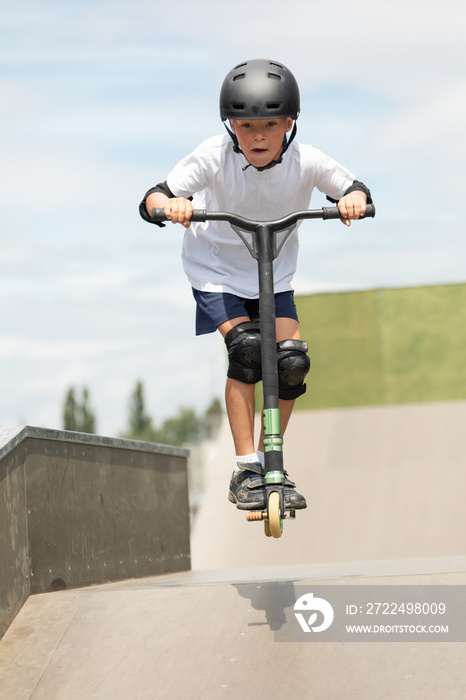 The boy jumps on a scooter.