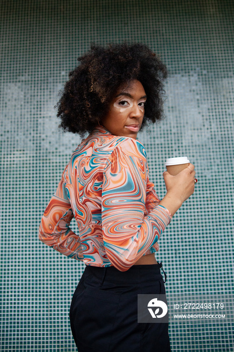 Curvy mixed-race woman with vitiligo posing in front of fun tiled wall with coffe-to-go