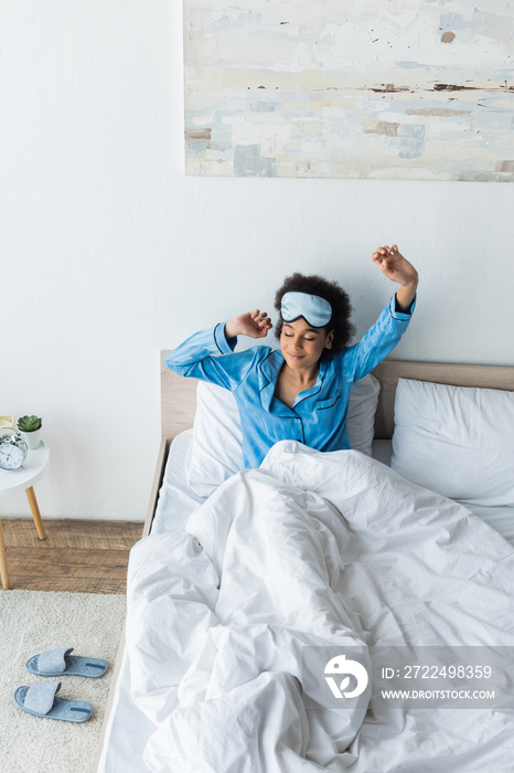 high angle view of pleased african american woman in sleeping mask stretching in bed