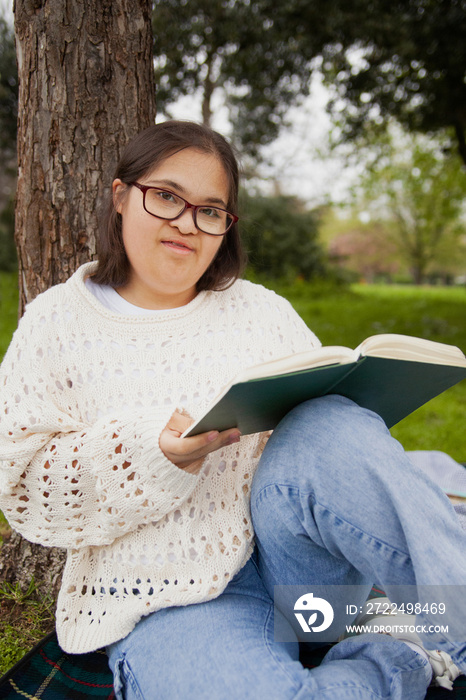 Curvy woman with Down syndrome reading in the park