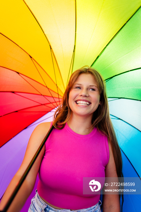 Happy beautiful pretty smiling young teen girl wearing bright pink top at colorful rainbow background. Trendy teenager generation Z lifestyle, pride month
