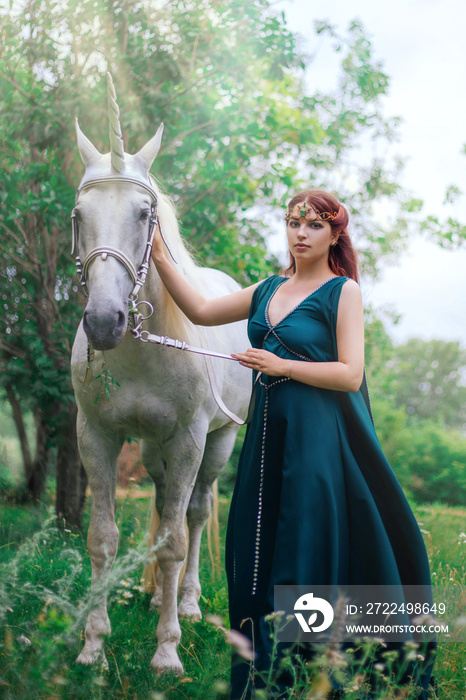 An elf with a unicorn. Beautiful girl in a green dress in nature with a white horse. Model in a medieval dress