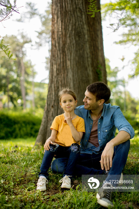 Single father sitting on grass by the tree with little daughter