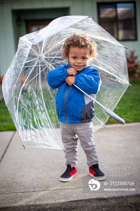 Cute little boy holding an umbrella as he leaves his home to go outside on a raining day. Smiling and ready to play despite the rainy weather