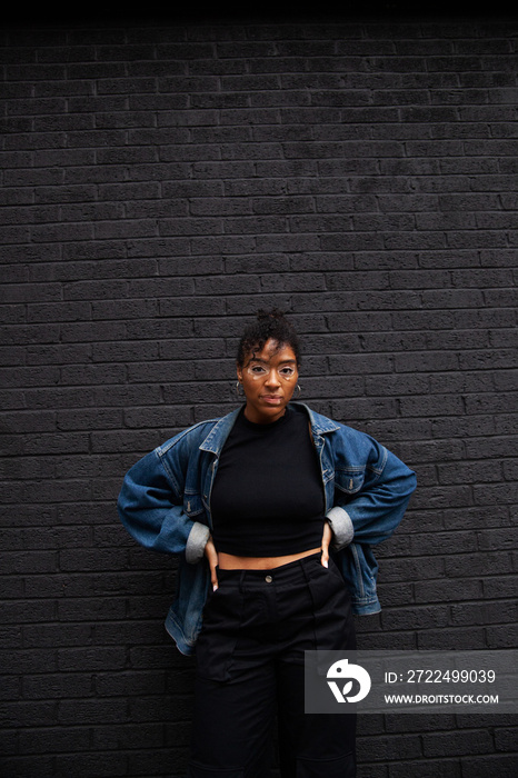 Mid-sized model with vitiligo posing in front of black wall and staring into the camera