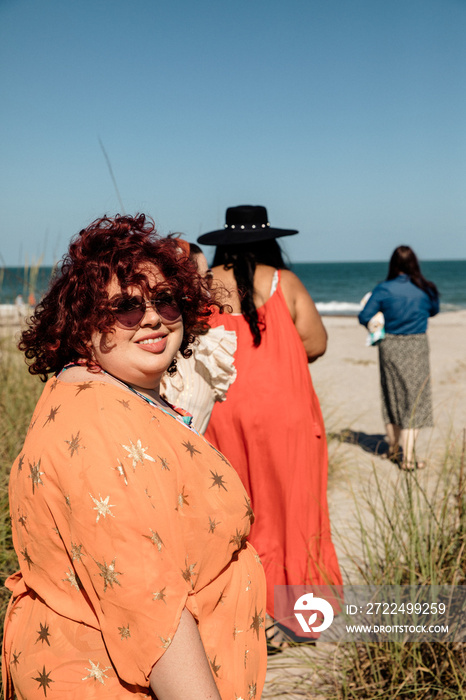 plus size woman looks at camera while friends walk towards beach