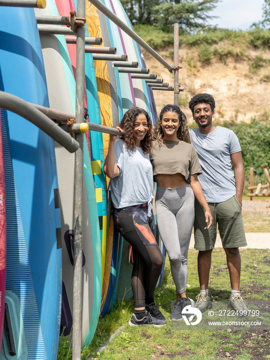 Portrait of smiling friends standing next to paddleboard rack