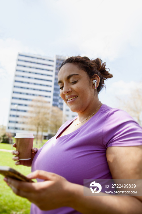 Young curvy woman wearing earbuds and holding coffee-to-go