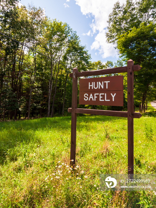 A wooden sign saying HUNT SAFELY on the side of a road in Warren county, Pennsylvania, USA on a sunny, summer day