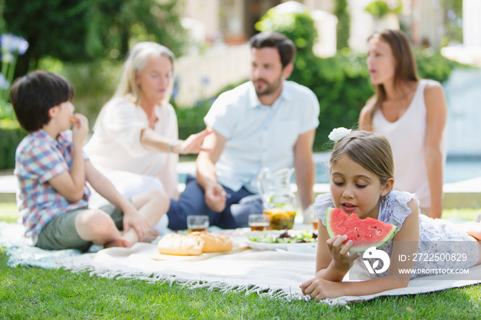 Girl eating watermelon on picnic blanket with family