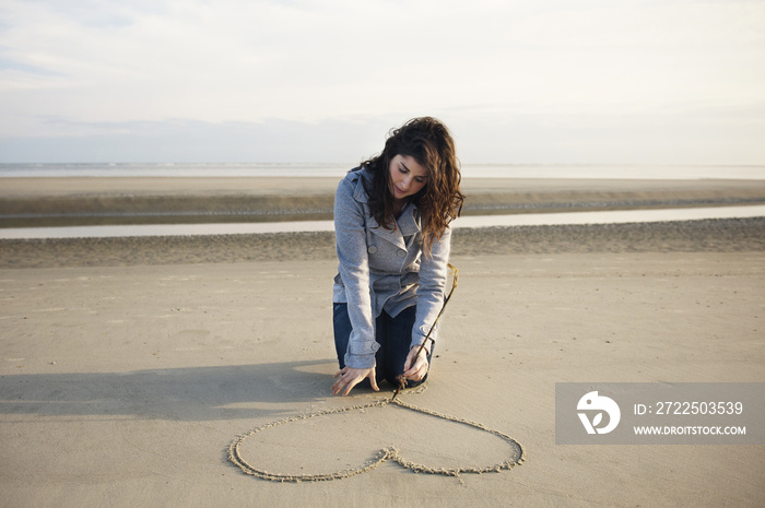 Woman drawing heart on sand at beach against sky