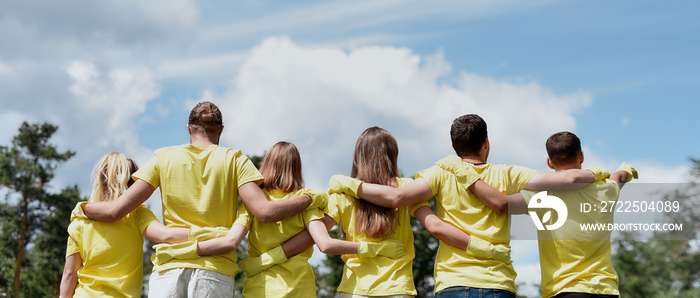 Love your nature. Group of young volunteers wearing uniform and rubber gloves hugging and looking at