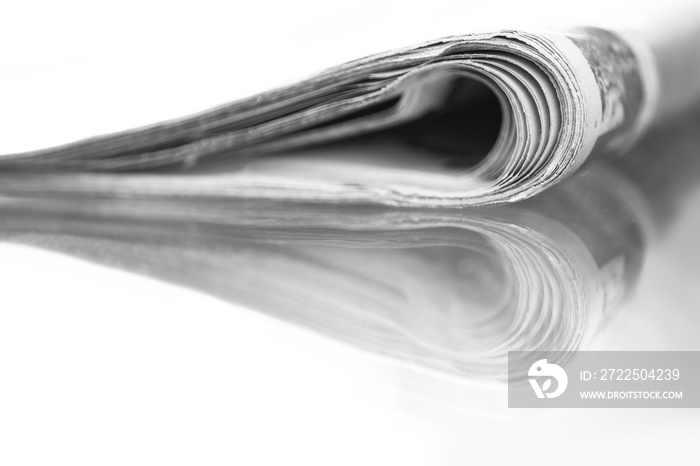 Folded newspaper mirrored on glass table, white background with narrow depth of field