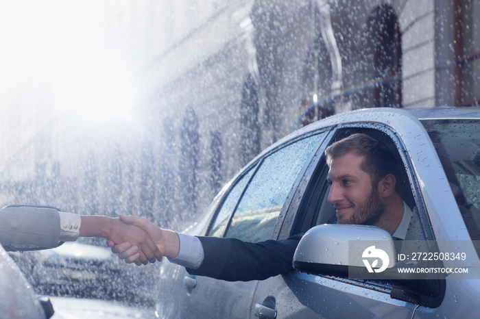 Businessmen shaking hands from cars on rain street