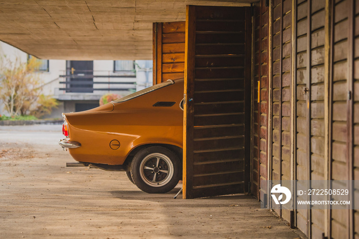 Old brown vintage car is being parked in a wooden car box parking. Rear of the car is visible going 