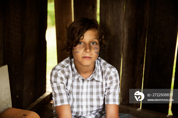 Portrait of boy with painted face sitting in wooden shed