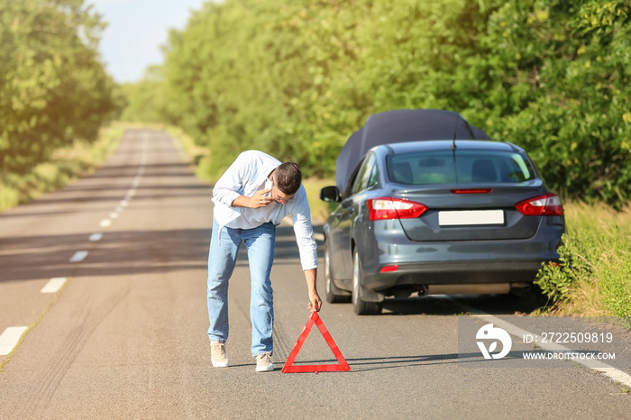 Young man with emergency stop sign near broken car on road