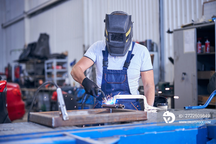 Male worker in welding helmet welding metal in garage