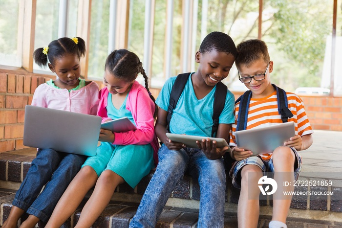 Kids sitting on staircase using laptop and digital tablet