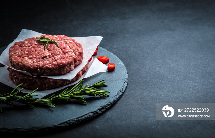 Raw burger cutlet from beef meat with garlic and rosemary on black background with copy space