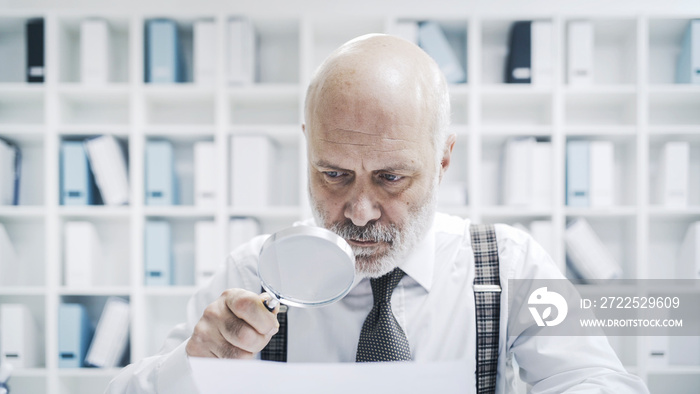 Corporate businessman checking paperwork with a magnifier