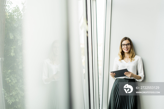 Young businesswoman standing wirth tablet in the office by window