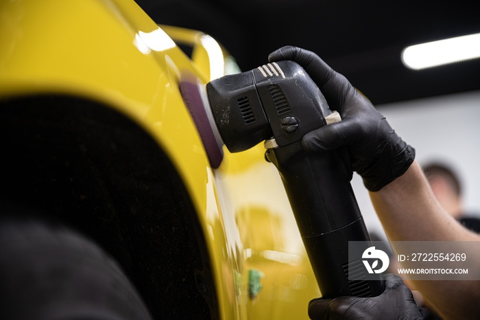 Man car detailing studio worker polishing yellow car varnish with electrical polisher