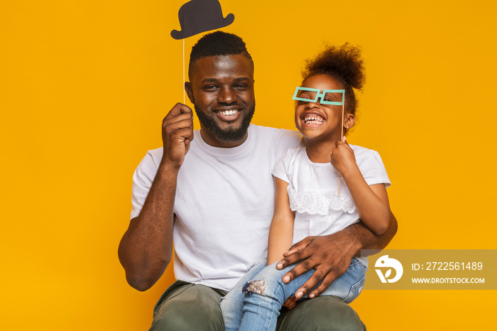 Cheerful afro father and daughter posing with photo props