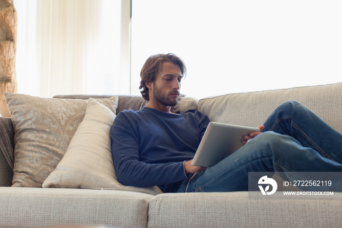 Young man with digital tablet relaxing on sofa