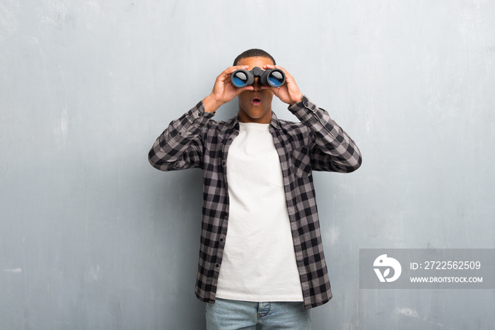 Young african american man with checkered shirt and looking for something in the distance with binoc