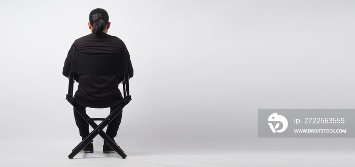 一个男人坐在黑色的导演椅上。这是白色背景。
