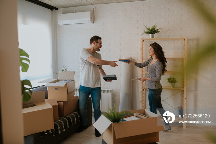 Photo of young couple unpacking boxes in new home on moving day. Young couple is sorting books.