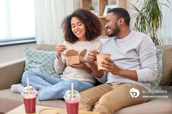 eating and people concept - happy african american couple with takeaway food and drinks at home