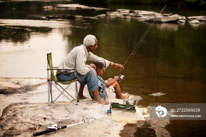 Boy and grandfather fishing in river