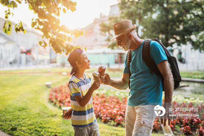 Happy grandfather enjoying with his grandson while eating ice cream outdoors in park.