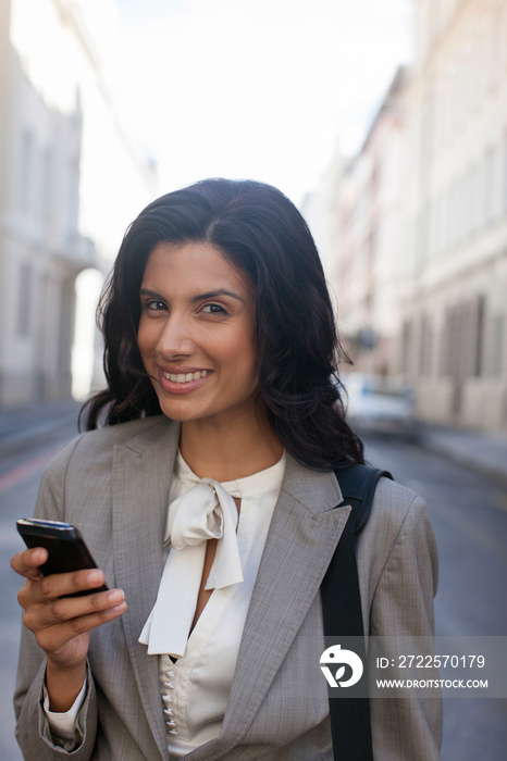 Portrait smiling businesswoman using smart phone on city street