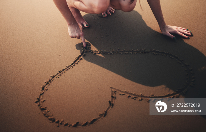 Closeup of hand drawing heart on sand