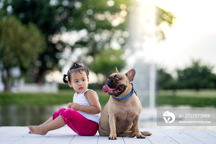 可爱的小女孩和她的法国斗牛犬坐在湖边。