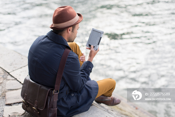 Man using digital tablet on ledge above river