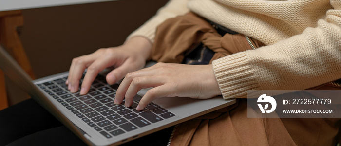 女性坐在办公室的办公椅上，用膝盖上的笔记本电脑打字