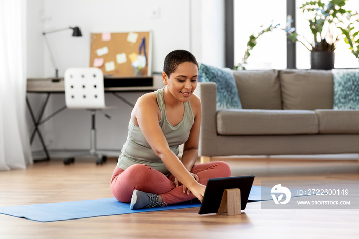 sport, fitness and technology concept - happy smiling young african american woman with tablet pc computer sitting on exercise mat at home