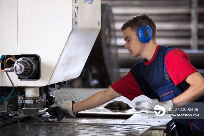 Inside a factory, industrial worker in action on metal press machine holding a steel piece ready to be worked.