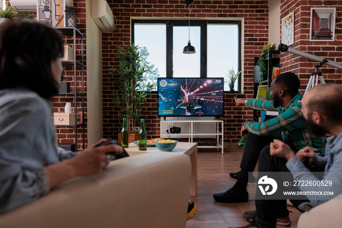 Diverse friends using tv console and joystick to play video games, having fun at house gathering with beer bottles. Group of people enjoying shooting competition with gaming strategy.