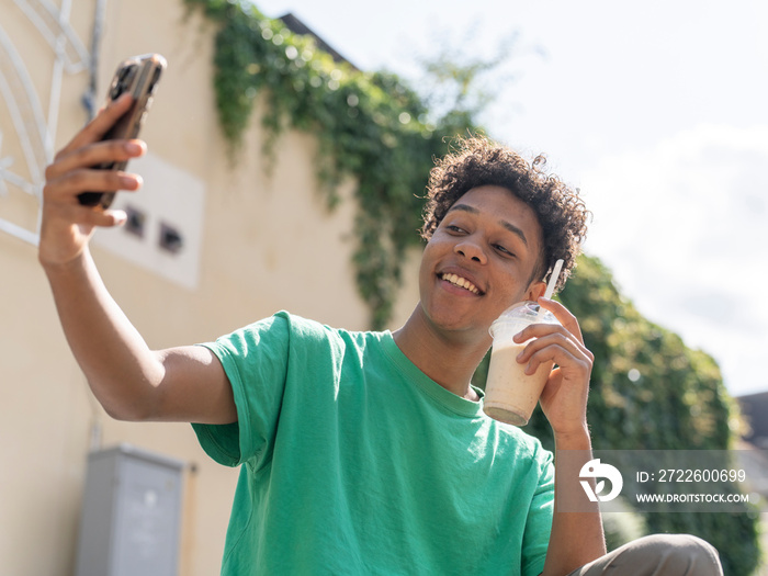 Young man taking selfie with smoothie on sunny day